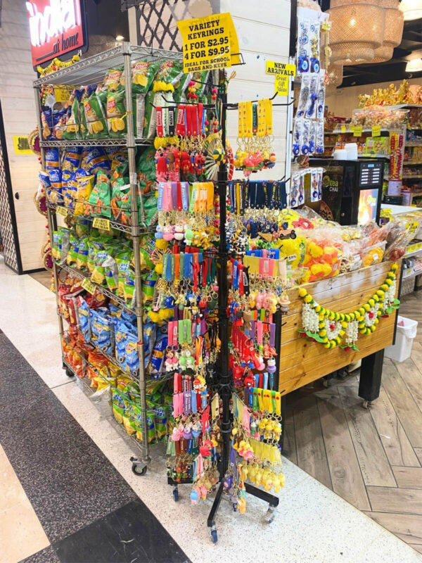 a black retail stand with colourful keyrings hanging off each prong and a yellow pricing sign on top, with other merchandise displayed in the background.