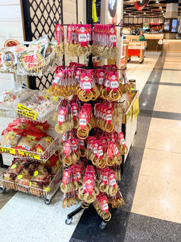 a black spinning stand on wheels at the front of a retail shop filled with gold bracelets with red tags.