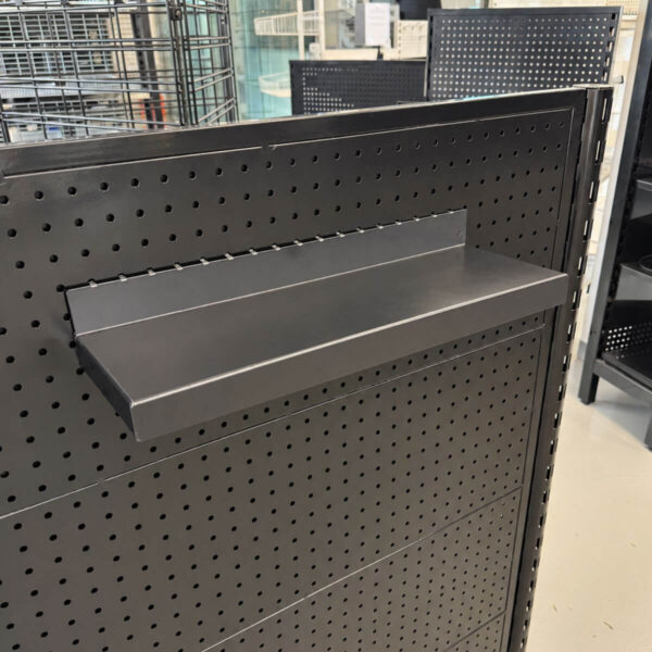 one small shelf in black attached to a pegboard shelving backing with retail shop fixtures in the background.
