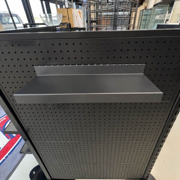 a small black shelf fixed to a pegboard shelving system with retail shop fixtures in the background.
